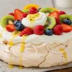 A classic pavlova topped with whipped cream, fresh strawberries, raspberries, blueberries, and sliced kiwi, drizzled with passion fruit sauce.